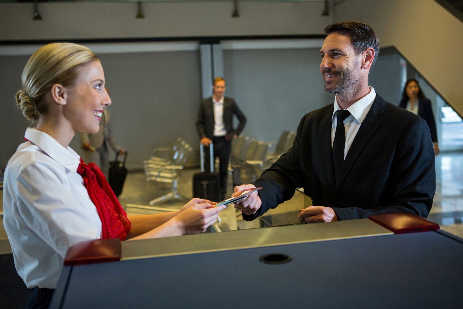 Female staff giving boarding pass to the businessman at the check in desk